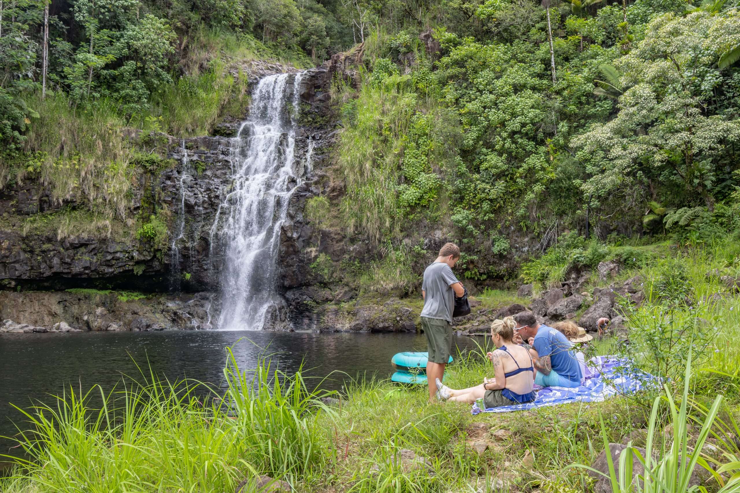 Kona waterfall tour stop at private waterfall location. Guests enjoying a picnic lunch at the base of the waterfall.